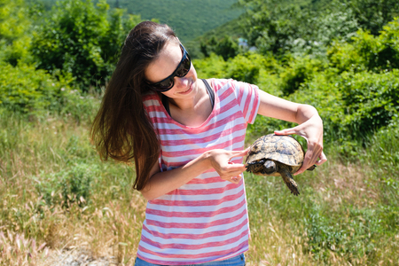 Close-up woman brunette in sunglasses and striped t-shirt keeping turtle in her hands in the forestの写真素材