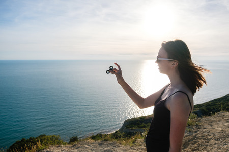 Young girl stands on a mountain with seascape, holds a spinner in her hand and looks at it.