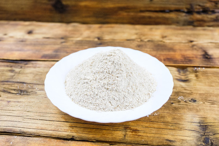 Close-up heap with wheat flour coarse in white plate on wooden background Left on the photoの写真素材