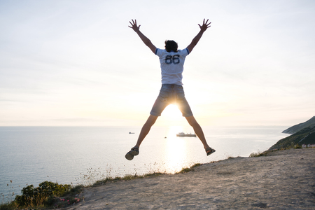 Man jumping on a mountain road with seascape at sunset. Back viewの写真素材