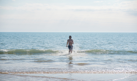 Unrecognizable man brunette in blue shorts runs out of the sea in the summer, sandy beach.の写真素材