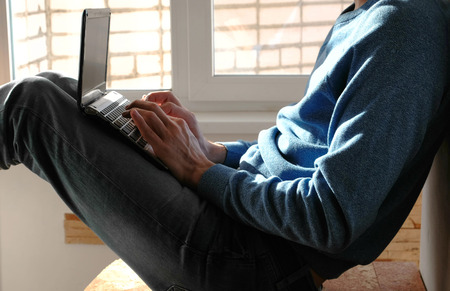 Working on laptop. Unrecognizable young man typing something in his laptop sitting on balcony near...