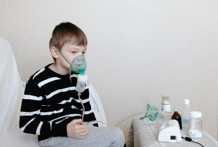 Use nebulizer and inhaler for the treatment. Boy inhaling through inhaler mask. Side view.の写真素材