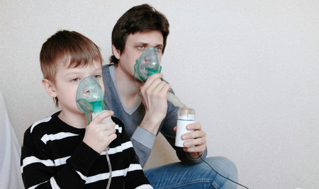 Use nebulizer and inhaler for the treatment. Man and boy inhaling through inhaler mask. Side view.の写真素材