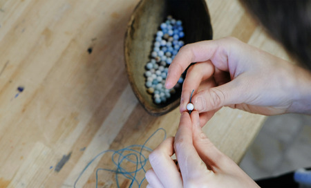 Weaving of beads. Close-up of a womans hands stringing beads on the thread, making jewelry in the...