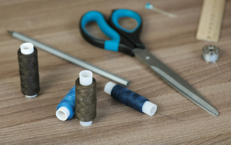 Sewing supplies scissors, thread, bobbins, pencil, a ruler on wooden table.