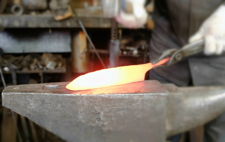 Making the knife out of metal at the forge. Close up blacksmiths hands taking a hammer and hitting hot metal on an anvil.の写真素材