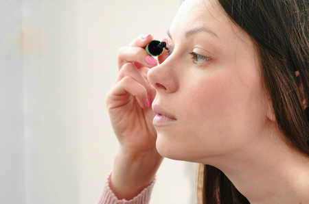 Young beautiful woman paints her eyes with mascara. Side view.