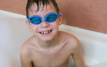 Boy 6-7 years sitting in the bubble bath with glasses for swimming. Looking at camera and smiling.の写真素材