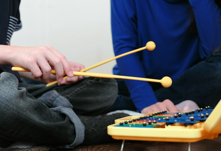 Playing music instrument. Closeup boys hand playing on xylophone and his mom sitting near him.