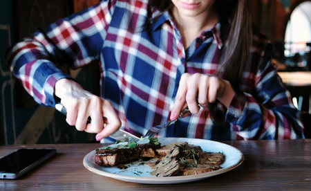 Closeup womans hand cutting piece of pork cooked on the coals with potatoes, gravy and greens on plate.の写真素材