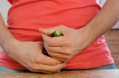 Man plays with a cucumber between his legs standing near the table. Cucumber closeup.