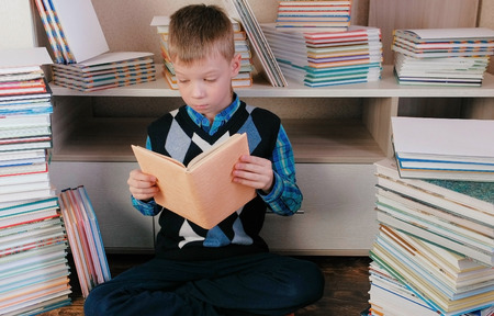 Boy reads a book sitting on the floor among the books.