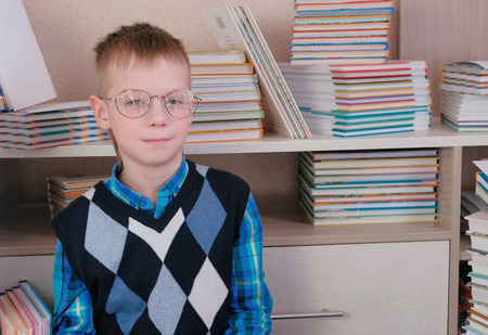 Tired seven-year-old boy with glasses sitting on the floor among the books.