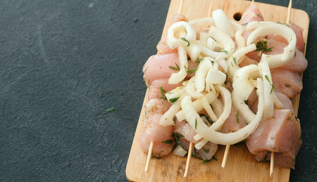 Closeup marinated shashlik from chicken meat on wooden skewer with onion on wood board.の写真素材