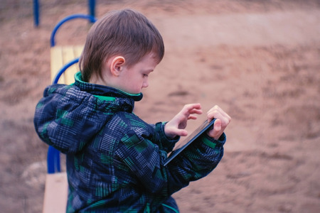 Boy touches a screen of tablet sitting in the Park on a bench. Side view.の写真素材