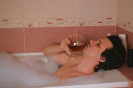 Man takes a bath and drinks cognac and crying. Depression and problems in life.の写真素材