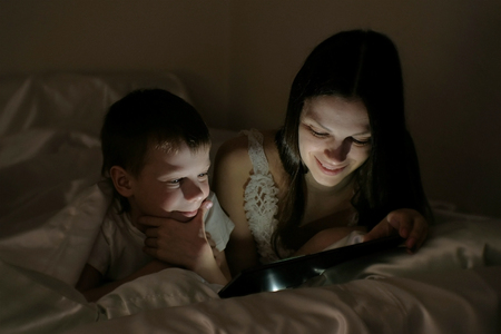Mom and son choose what to watch before going to bed on the tablet under the blanket.の写真素材