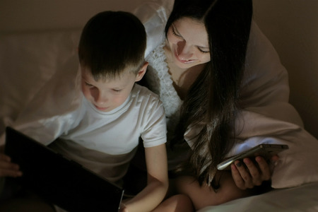 Young woman mom and her son watching interesting film together on tablet and laugh under the...