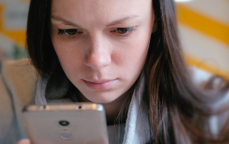 Young seriously woman reading something on her mobile phone sitting in cafe. Closeup face.の写真素材