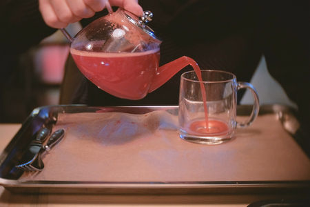 Man pours some cranberry tea from teapot to cup. Close-up man's handsの写真素材