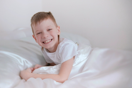 Seven-year-old boy just woke up and laughs while lying in bed.の写真素材