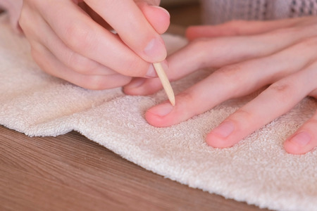 Woman cleans excess nail Polish using wooden orange stick for manicure.の写真素材