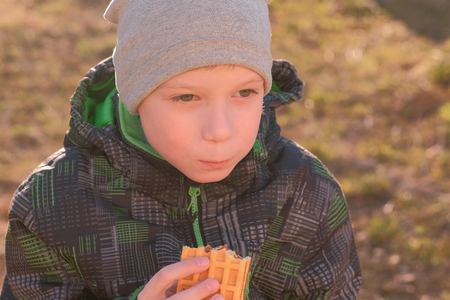 Boy eats waffles sitting on the bench in park. Front view.の写真素材