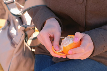 Close-up womans hands peels tangerine in park.の写真素材