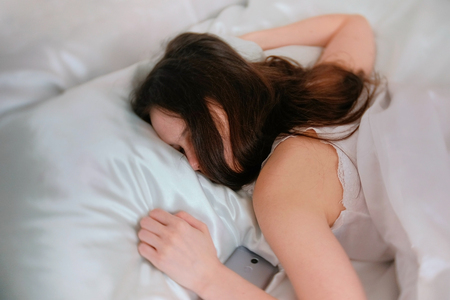 Young woman brunette sleeping in bed. Mobile phone near her.の写真素材