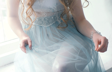 Unrecognizable young slim sexy blond girl sitting in lingerie and blue boudoir. Front view. Closeup body.の写真素材