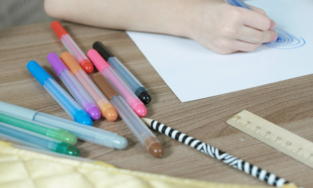 Close-up of the child's hands draw ovals with a blue marker on white paper.