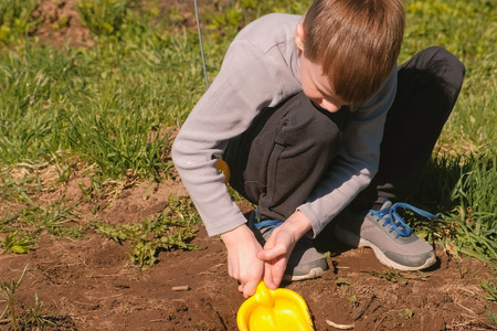 Boy digs the ground with a yellow plastic shovel on the lawn near the house.