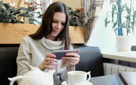 Young woman brunette pictures of teapot and Cup in a cafe on her cell phone. Front view.