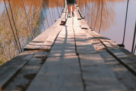 Close-up legs of family mom, dad and daughter walk on the old suspension bridge over the river.