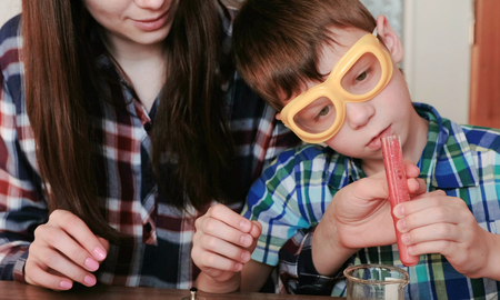 Chemistry experiments at home. Mom and son make a chemical reaction with the release of gas in the test tube with red liquid.の写真素材