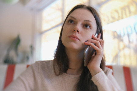 Young beautiful woman brunette calls and waits answer in her mobile phone in cafe and waiting her friends.の写真素材