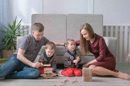 Family mom, dad and two twin brothers play together building out of wooden blocks on the floor.の写真素材