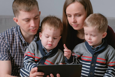 Family with tablet. Mom, dad and two sons twins looking at tablet sitting in sofa.の写真素材
