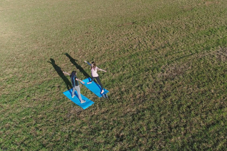 Two girls stretching on mats on the field. Aerial panoramic view. Making yoga exersices.の写真素材