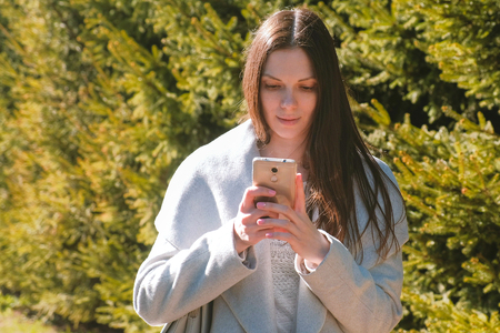 Portrait of beautiful brunette sending a message in her phone in park. Side view.の写真素材