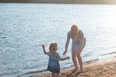 Beautiful blonde mom and daughter run towards each other on the river Bank at sunset.の写真素材