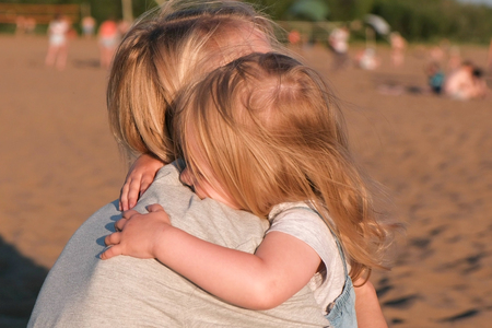 Beautiful blonde mom and daughter cuddling on the beach at sunset.の写真素材