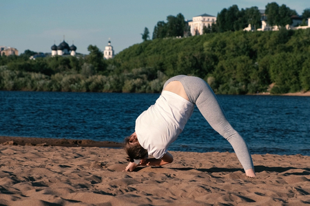 Woman stretching yoga on the beach by the river in the city. Beautiful view.の写真素材