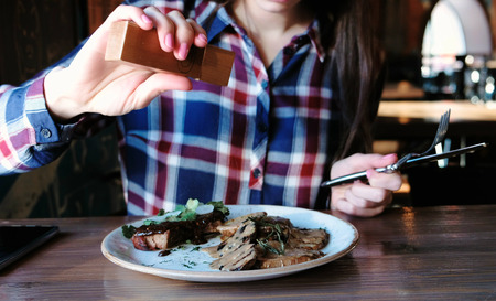 Closeup womans hand pepper piece of pork cooked on the coals with potatoes, gravy and greens on plate.の写真素材