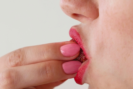 Woman with red lips eats strawberries. Mouth close-up. Side view.の写真素材