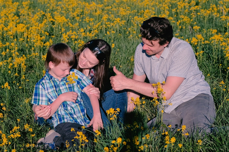 Mother, father and son play with yellow flowers sitting in the grass. Family walk.の写真素材