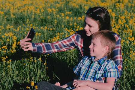 Mom and son make selfie on the phone sitting on the grass among the yellow flowers.の写真素材