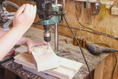 Worker drills holes in wooden templates. Manufacture of wooden toys. Close-up hands.の写真素材