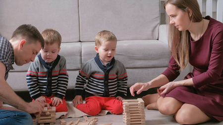 Family mom, dad and two twin brothers play together building out of wooden blocks on the floor.の写真素材